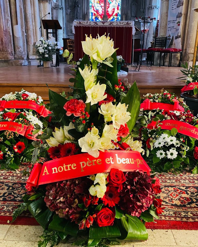 Composition de deuil aux amaryllis blanches, roses rouges et hortensia bordeaux, ornée d’un ruban, dans une église