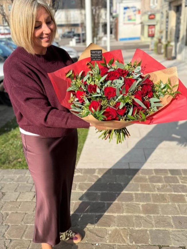 Claire tenant un grand bouquet de roses rouges enveloppé de kraft et de papier rouge